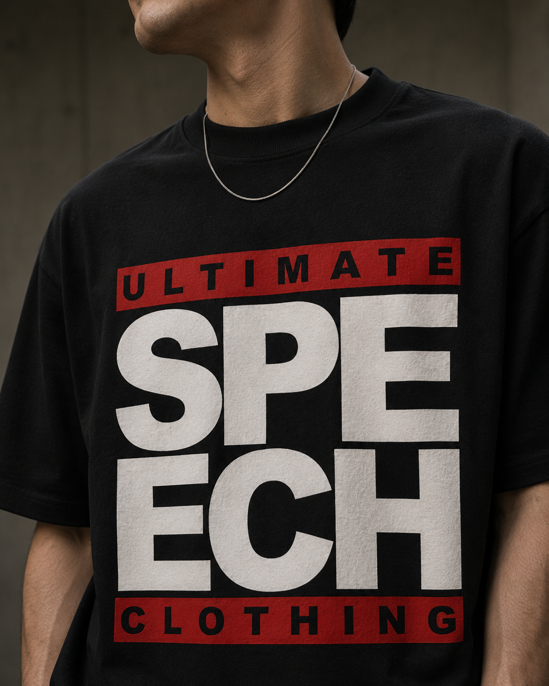 A close-up of a person wearing a black graphic T-shirt with large white block letters reading 'SPEECH' and red bars above and below reading 'ULTIMATE' and 'CLOTHING'.