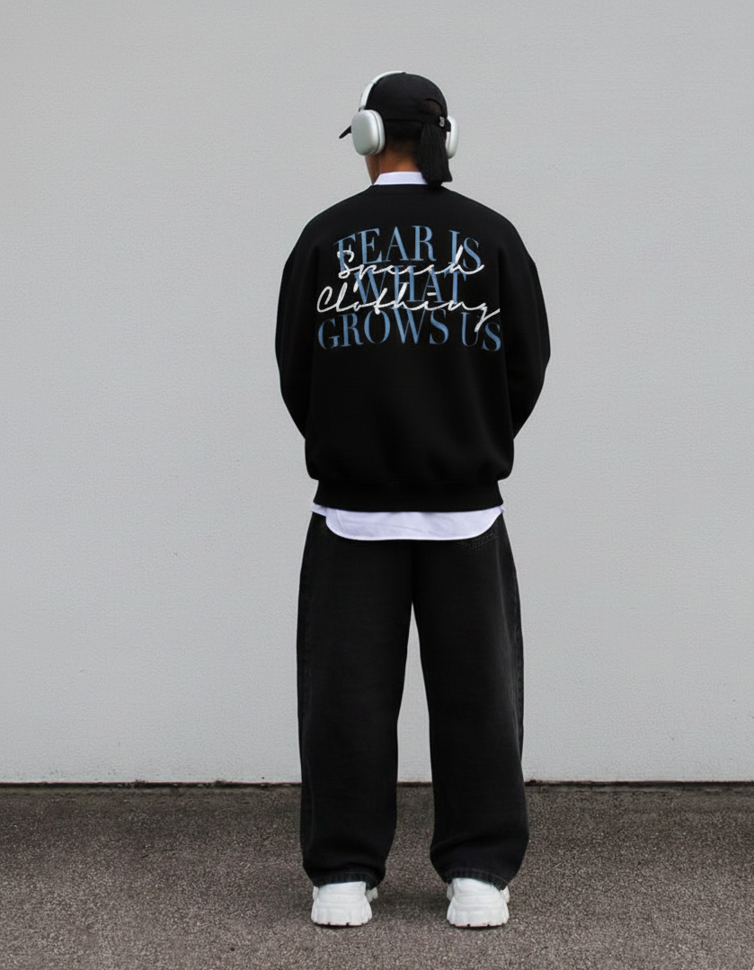 Person wearing a black tracksuit with text on the back against a plain wall.