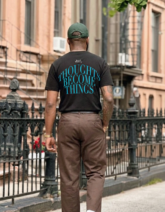 Man walking on a street wearing a black t-shirt with text and brown pants.