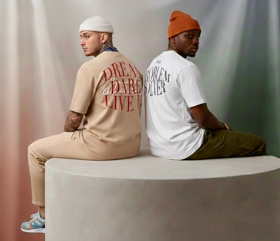 Two people sitting on a white block, wearing t-shirts with text designs.