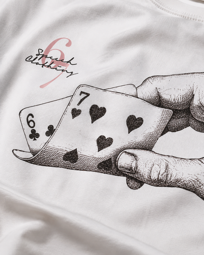 White t-shirt featuring a black ink sketch of a hand holding playing cards (6 of clubs and 7 of hearts) with a pink 'Squad Editing' logo printed on the chest.