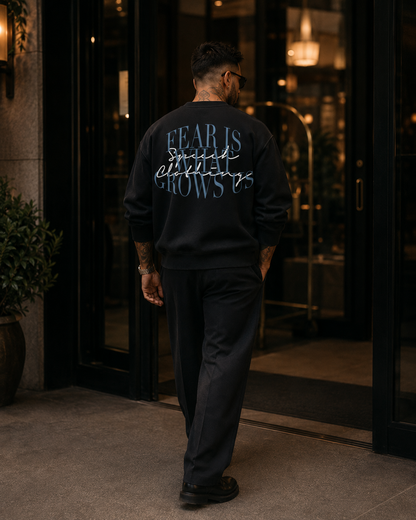 A man viewed from behind wearing a black crewneck sweatshirt with a graphic text print on the back, walking through a glass door entrance.