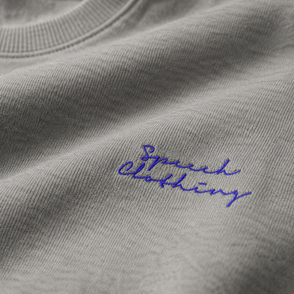 Close-up of a light gray heather crewneck sweatshirt with blue embroidered script reading 'Speech Clothing' on the chest.