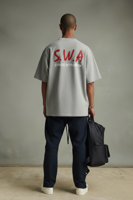 Person wearing a gray heavyweight  t-shirt with 'S.W.A.' on the back, holding a black bag against a plain background.