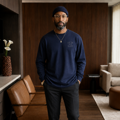 A man wearing a navy blue long-sleeve crewneck sweatshirt with 'NOT THE AGE, BUT THE WHO' printed on the chest, paired with dark gray trousers and a navy beanie, standing in a modern, warm-toned interior room.